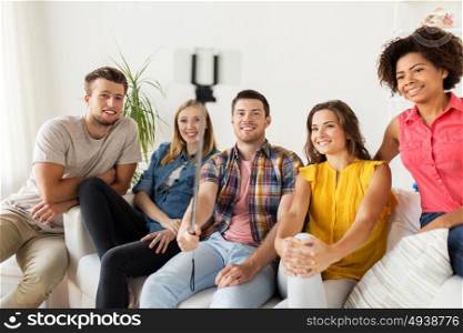 friendship, and people concept - group of happy friends taking picture with smartphone and selfie stick at home. happy friends taking selfie by smartphone at home