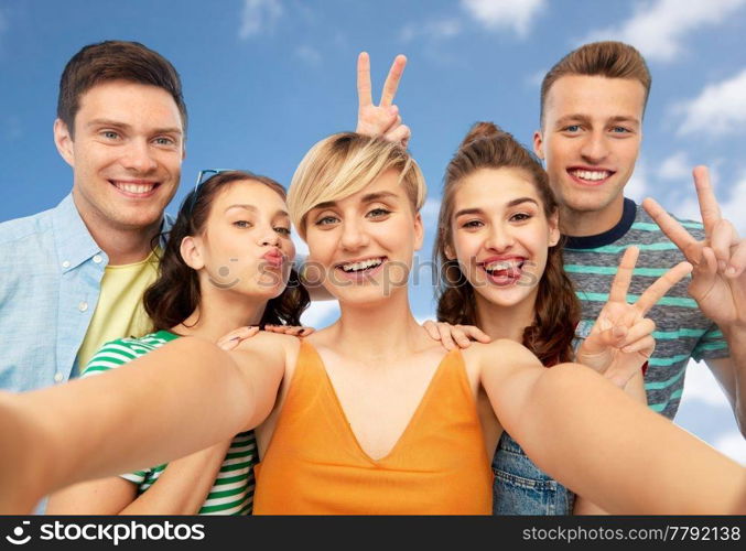 friendship and people concept - group of happy smiling friends taking selfie and showing peace hand sign over blue sky and clouds background. happy friends taking selfie and showing peace