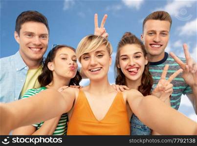 friendship and people concept - group of happy smiling friends taking selfie and showing peace hand sign over blue sky and clouds background. happy friends taking selfie and showing peace