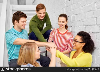 friendship and people concept - smiling teenage friends or students stacking hands hanging out on stairs. teenage friends or students stacking hands