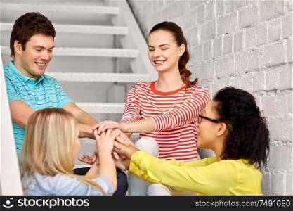 friendship and people concept - smiling teenage friends or students stacking hands hanging out on stairs. teenage friends or students stacking hands