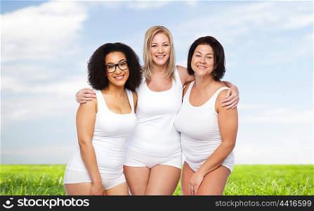 friendship, beauty, body positive and people concept - group of happy plus size women in white underwear over blue sky and grass background