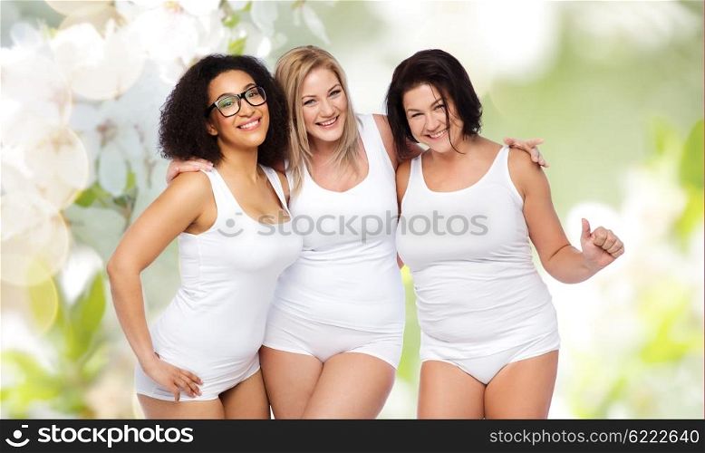 friendship, beauty, body positive and people concept - group of happy plus size women in white underwear over natural spring cherry blossom background