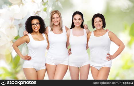 friendship, beauty, body positive and people concept - group of happy women different in white underwear over natural spring cherry blossom background