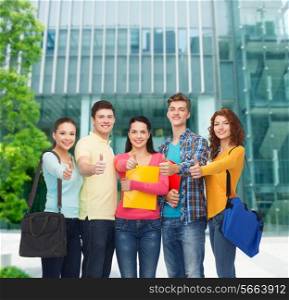 friendship, business, education and people concept - group of smiling teenagers with folders and school bags showing thumbs up over campus background