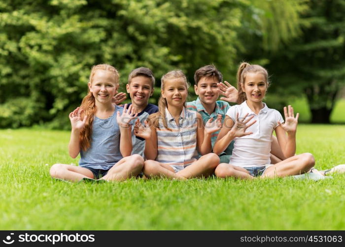 friendship, childhood, leisure and people concept - group of happy kids or friends waving hands in summer park