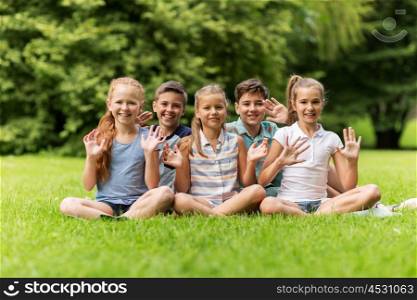 friendship, childhood, leisure and people concept - group of happy kids or friends waving hands in summer park