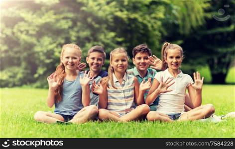 friendship, childhood, leisure and people concept - group of happy kids or friends waving hands in summer park. group of happy kids waving hands outdoors