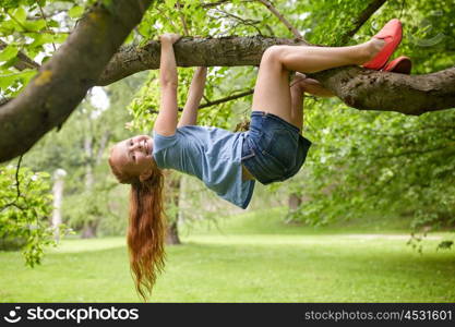 friendship, childhood, leisure and people concept - happy smiling little redhead girl hanging upside down on tree in summer park