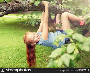 friendship, childhood, leisure and people concept - happy smiling little redhead girl hanging upside down on tree in summer park. happy little girl hanging on tree in summer park