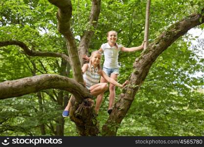 friendship, childhood, leisure and people concept - two happy girls climbing up tree and having fun in summer park