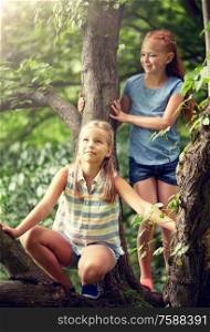 friendship, childhood, leisure and people concept - two happy girls climbing up tree and having fun in summer park. two happy girls climbing up tree in summer park