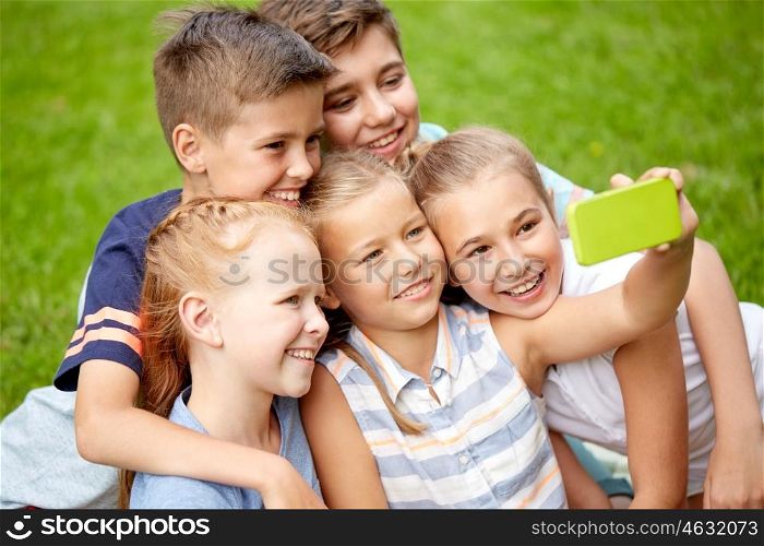 friendship, childhood, technology and people concept - group of happy kids or friends taking selfie by smartphone in summer park