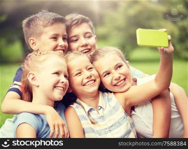friendship, childhood, technology and people concept - group of happy kids or friends taking selfie by smartphone in summer park. happy kids or friends taking selfie in summer park