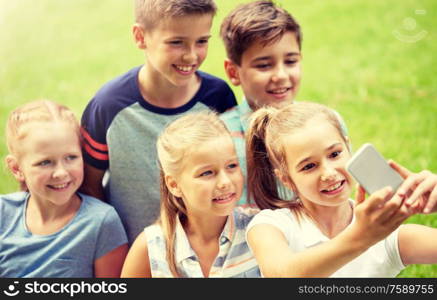 friendship, childhood, technology and people concept - group of happy kids or friends taking selfie by smartphone in summer park. happy kids or friends taking selfie in summer park