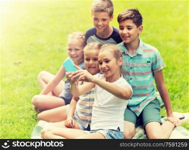 friendship, childhood, technology and people concept - group of happy kids or friends taking selfie by smartphone in summer park. happy kids or friends taking selfie in summer park