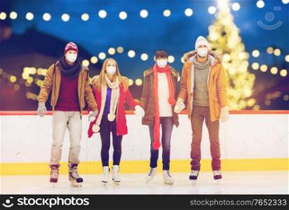 friendship, christmas and leisure concept - friends wearing face protective medical masks for protection from virus disease holding hands at outdoor skating rink over holiday lights background. friends in masks on christmas skating rink