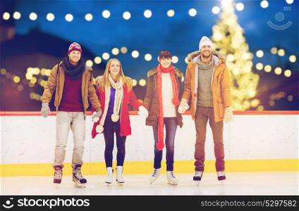 friendship, christmas and leisure concept - happy friends holding hands on skating rink over outdoor holiday lights background. happy friends on christmas skating rink
