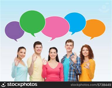 friendship, communication, gesture and people concept - group of smiling teenagers showing ok sign over blue background with text bubbles