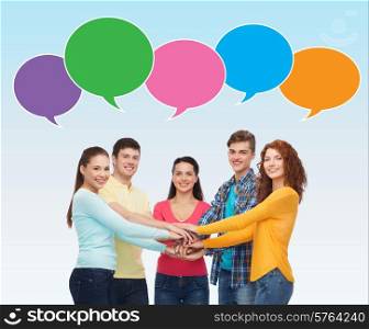 friendship, communication, gesture and people concept - group of smiling teenagers with hands on top of each other over blue background with text bubbles