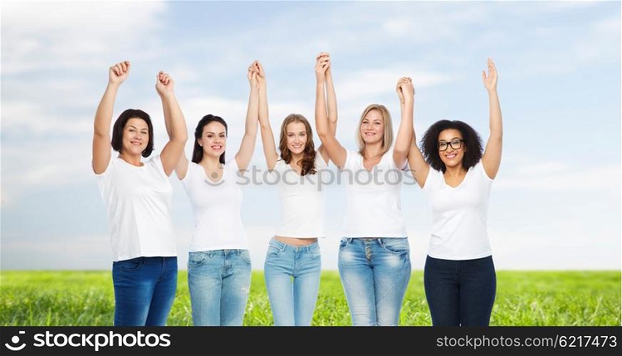 friendship, diverse, body positive and people concept - group of happy different size women in white t-shirts holding hands up over blue sky and grass background