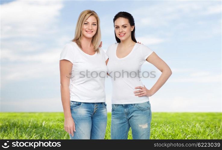 friendship, diverse, body positive and people concept - group of happy different women in white t-shirts hugging over blue sky and grass background