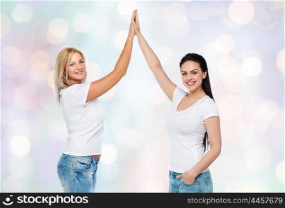 friendship, diverse, body positive, gesture and people concept - group of happy different women in white t-shirts making high five over holidays lights background