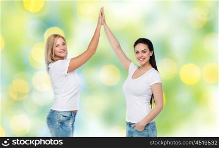 friendship, diverse, body positive, gesture and people concept - group of happy different women in white t-shirts making high five over green holidays lights background