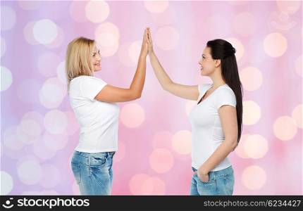 friendship, diverse, body positive, gesture and people concept - group of happy different women in white t-shirts making high five over rose quartz and serenity holidays lights background
