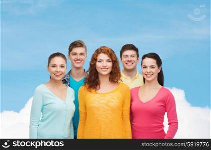 friendship, dream and people concept - group of smiling teenagers standing over blue sky with white cloud background