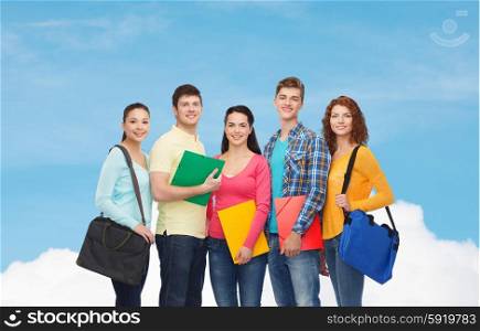 friendship, dream, education and people concept - group of smiling teenagers with folders and school bags over blue sky with white cloud background