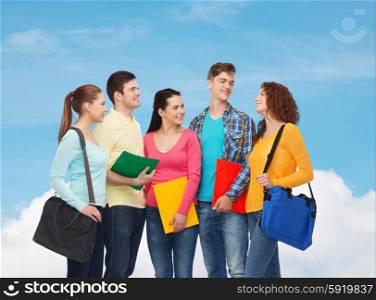 friendship, dream, education and people concept - group of smiling teenagers with folders and school bags over blue sky with white cloud background