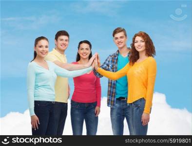friendship, dream, teamwork, gesture and people concept - group of smiling teenagers making high five over blue sky with white cloud background