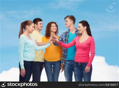 friendship, dream, teamwork, gesture and people concept - group of smiling teenagers making high five over blue sky with white cloud background