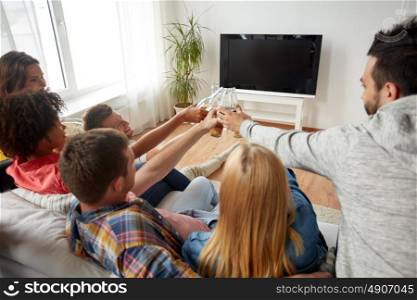 friendship, drink, alcohol, holidays and people concept - happy friends clinking beer bottles and watching tv at home. friends clinking beer and watching tv at home