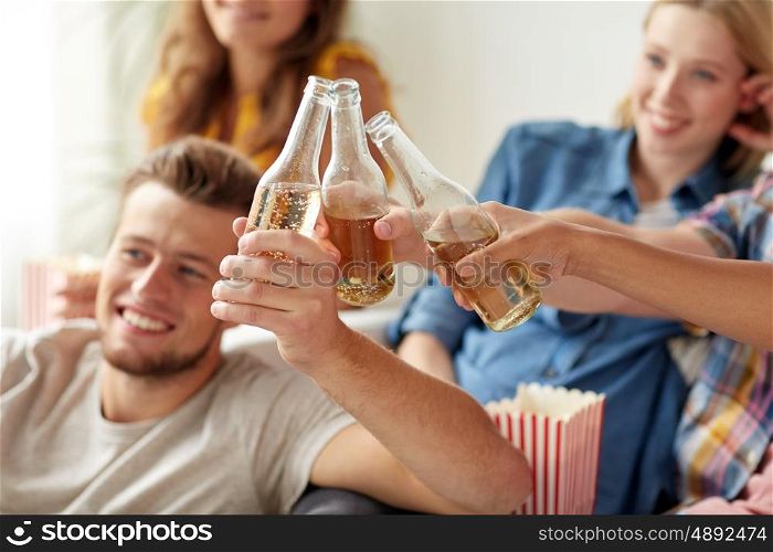 friendship, drink, alcohol, holidays and people concept - happy friends clinking beer bottles at home party