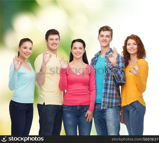 friendship, ecology, gesture and people concept - group of smiling teenagers showing ok sign over green background