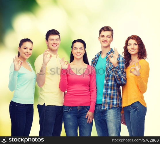 friendship, ecology, gesture and people concept - group of smiling teenagers showing ok sign over green background