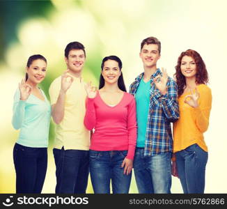 friendship, ecology, gesture and people concept - group of smiling teenagers showing ok sign over green background