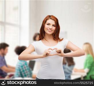 friendship, education and happy people concept - smiling girl in white t-shirt showing heart with hands