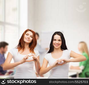 friendship, education and happy people concept - two smiling girls in white t-shirts showing heart with hands