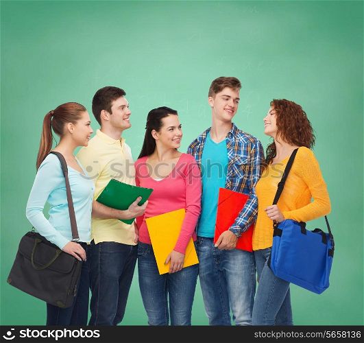 friendship, education and people concept - group of smiling teenagers with folders and school bags over green board background