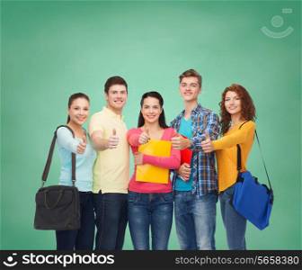 friendship, education and people concept - group of smiling teenagers with folders and school bags showing thumbs up over green board background