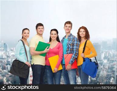 friendship, education and people concept - group of smiling teenagers with folders and school bags over city background