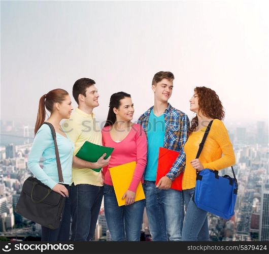 friendship, education and people concept - group of smiling teenagers with folders and school bags over city background