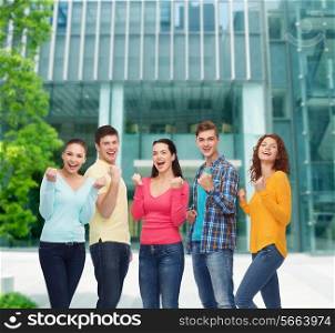 friendship, education, business, gesture and people concept - group of smiling teenagers showing triumph gesture over campus background