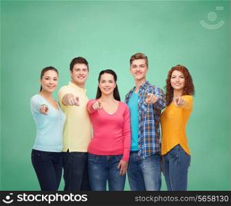 friendship, education, school and people concept - group of smiling teenagers pointing finger on you over green board background