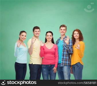 friendship, education, school and people concept - group of smiling teenagers showing ok sign over green board background