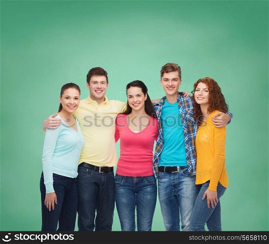 friendship, education, school and people concept - group of smiling teenagers standing and hugging over green board background