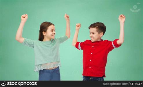 friendship, education, school, gesture and people concept - happy smiling boy and girl raising fists and celebrating victory over green chalk board background
